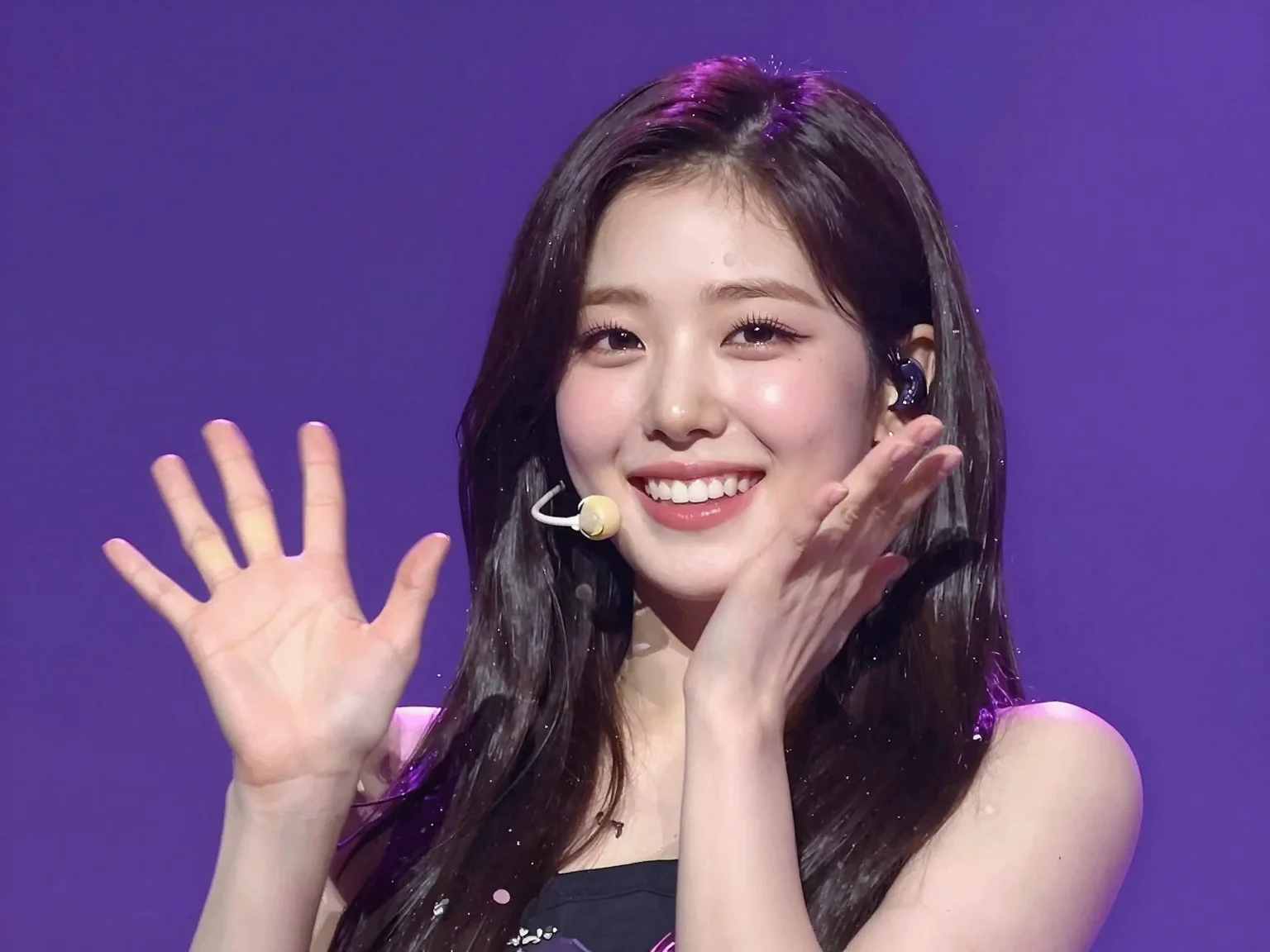 An illustration of a Korean female idol resembling TWICE's Tzuyu, looking at the viewer on stage and waving with both hands with a very happy smile that is a mixture of surprise and embarrassment. She is 18 years old, and the overall color scheme is a bit purple.