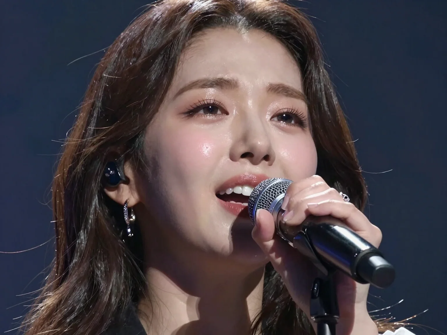 A Korean female idol: Close-up of a female singer’s face, emotion pouring out as she sings into a microphone, intense focus and passion visible, soft stage lighting casting dramatic shadows, detailed expression in high definition, panoramic view, idol photoshoot style